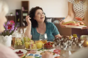אישה בגיל המעבר צוחקת סביב שולחן ארוחה עם חברות