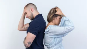 זוג עומד גב אל גב על רקע לבן, שניהם מחזיקים את הראש בידיים בהבעה עייפה, אחרי ריב
