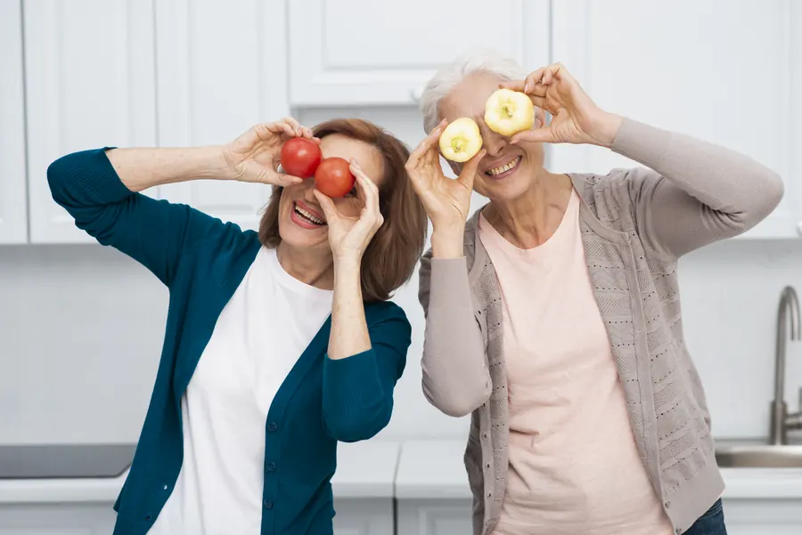 שתי נשים בגיל המעבר צוחקות במטבח עם עגבניות ופלפלים